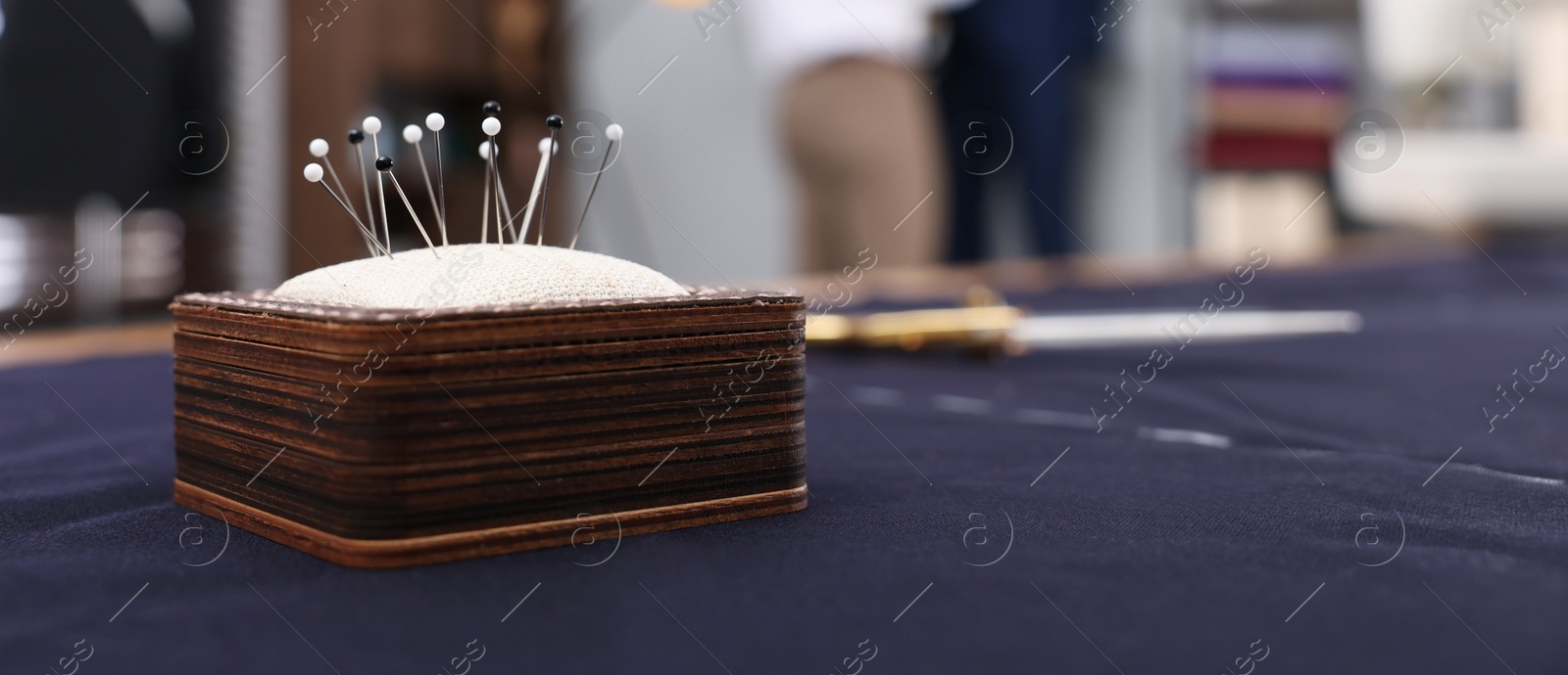 Image of Pin cushion and purple fabric on table in dressmaking workshop, closeup. Banner design with space for text