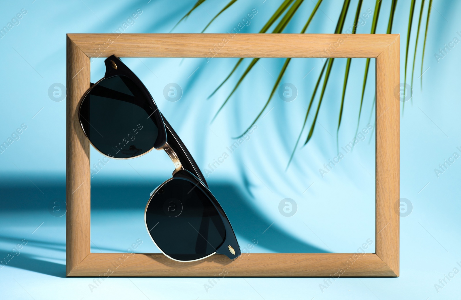 Photo of Stylish sunglasses near photo frame on light blue background