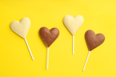 Different chocolate heart shaped lollipops on yellow background, flat lay