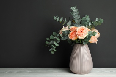 Bouquet of beautiful flowers and eucalyptus branches in vase on white wooden table against black background. Space for text