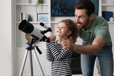 Photo of Little girl with his father looking at stars through telescope in room