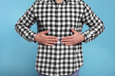 Photo of Man suffering from stomach pain on light blue background, closeup