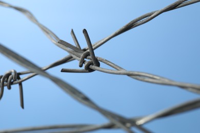 Metal barbed wire on light blue background, closeup