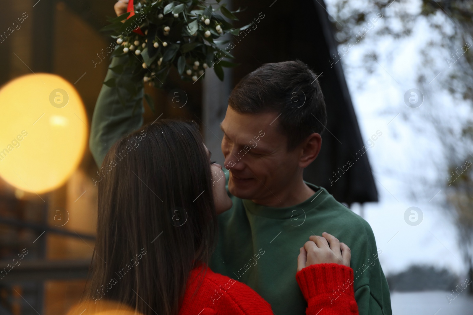 Photo of Happy couple standing under mistletoe bunch outdoors