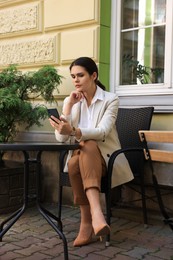 Photo of Beautiful young woman using smartphone at table in outdoor cafe