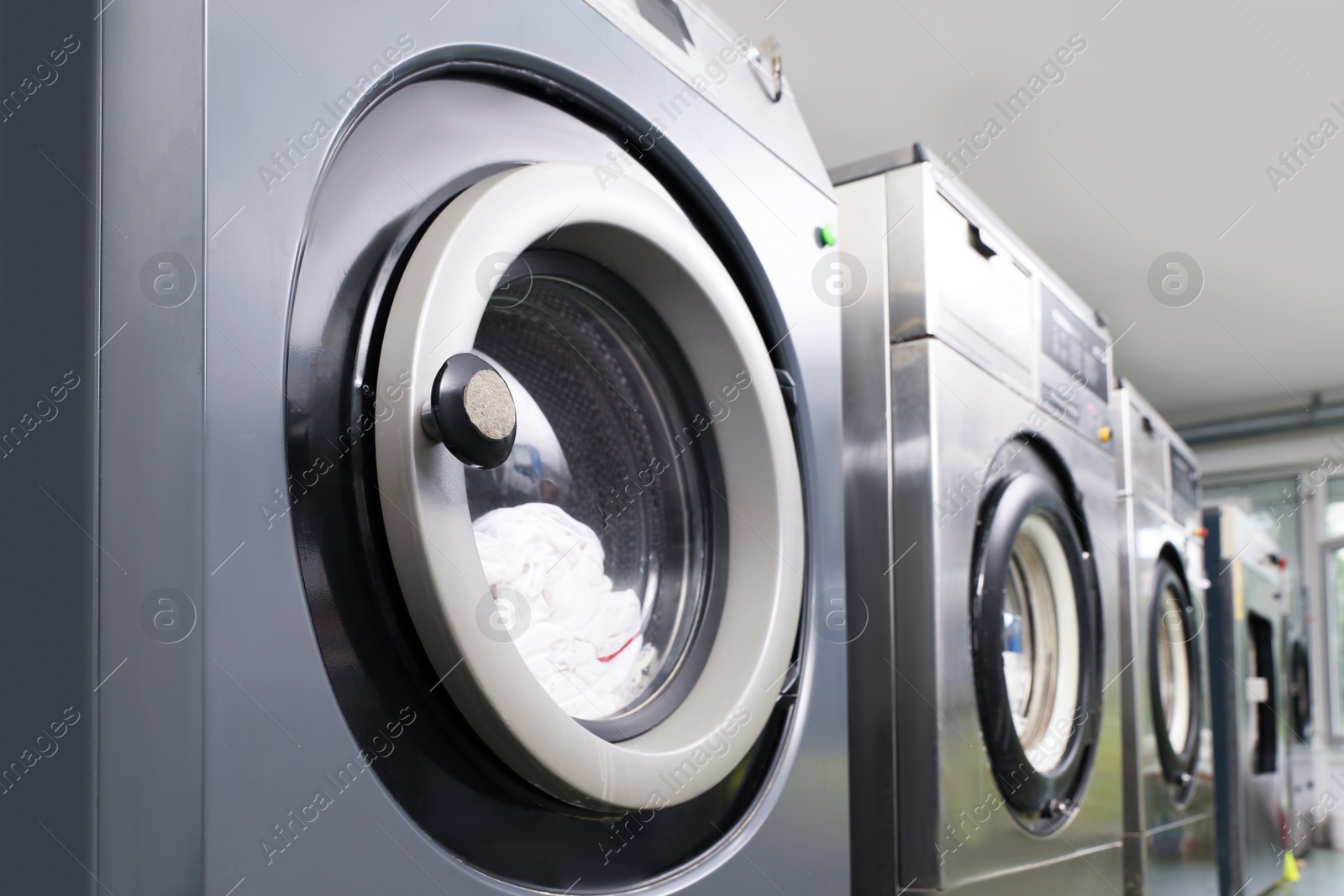 Photo of Row of modern washing machines in dry-cleaning, closeup