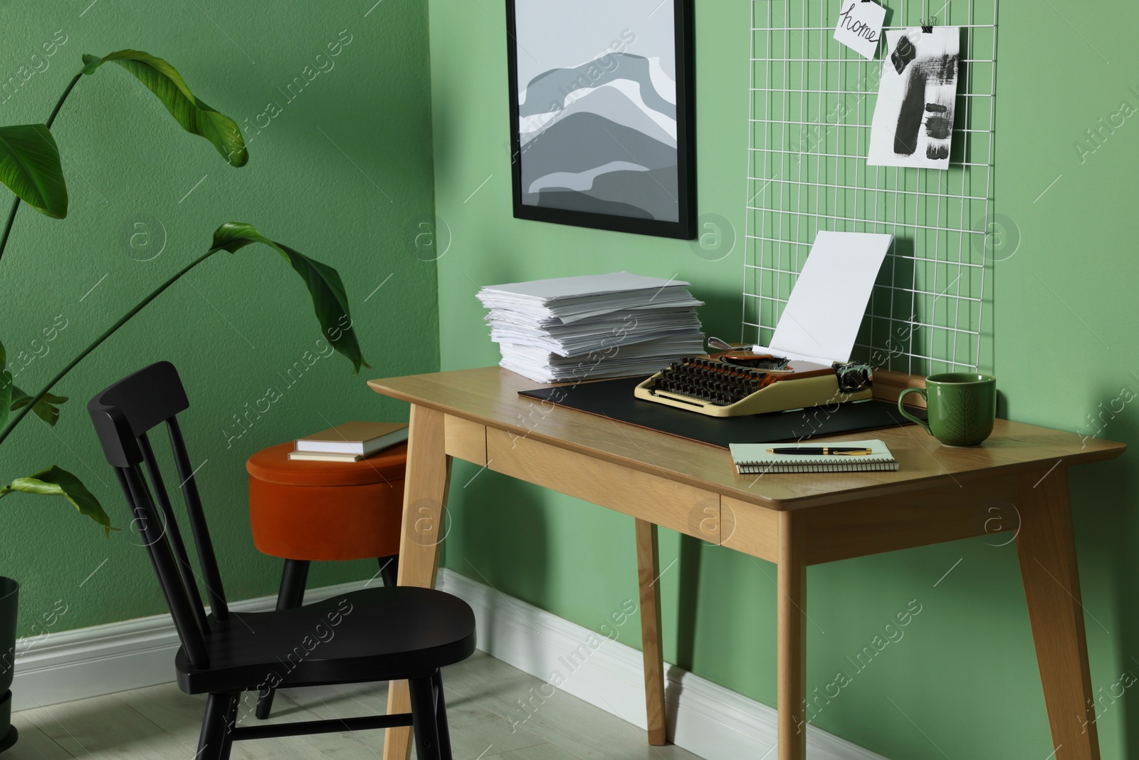 Photo of Typewriter, stack of papers and mood board on wooden table near pale green wall. Writer's workplace