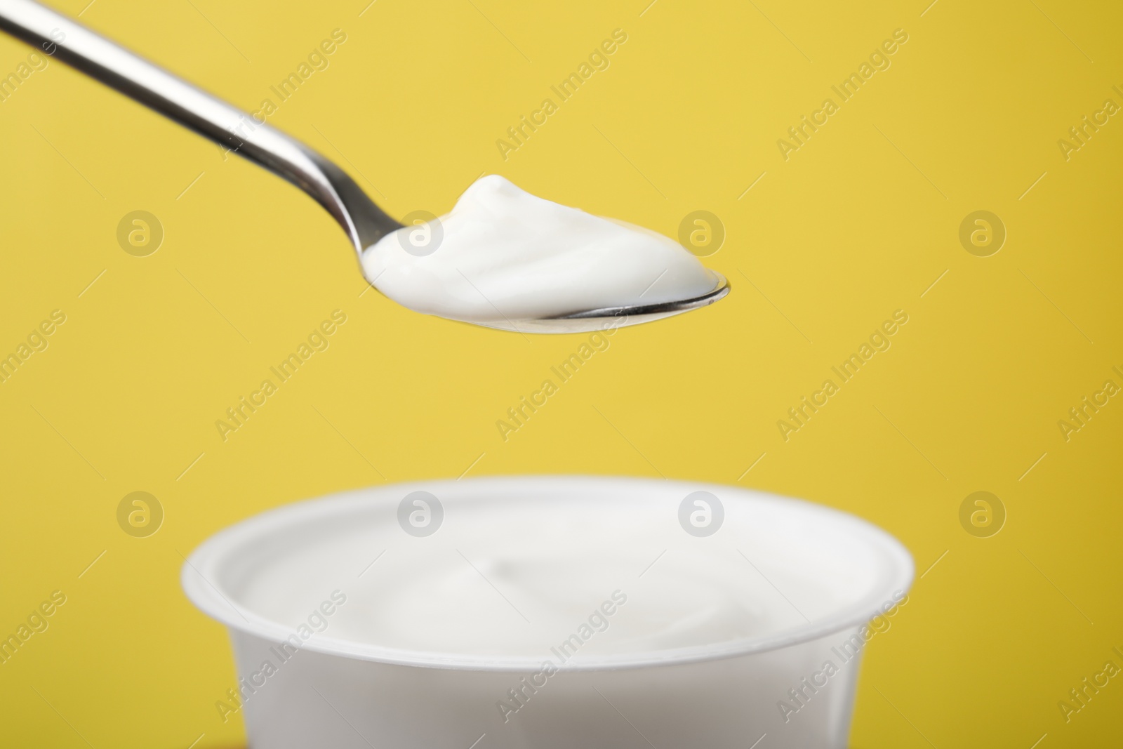 Photo of Eating delicious natural yogurt on yellow background, closeup