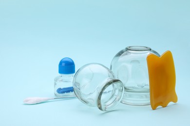 Photo of Glass cups and other equipment for cupping therapy on light blue background. Space for text