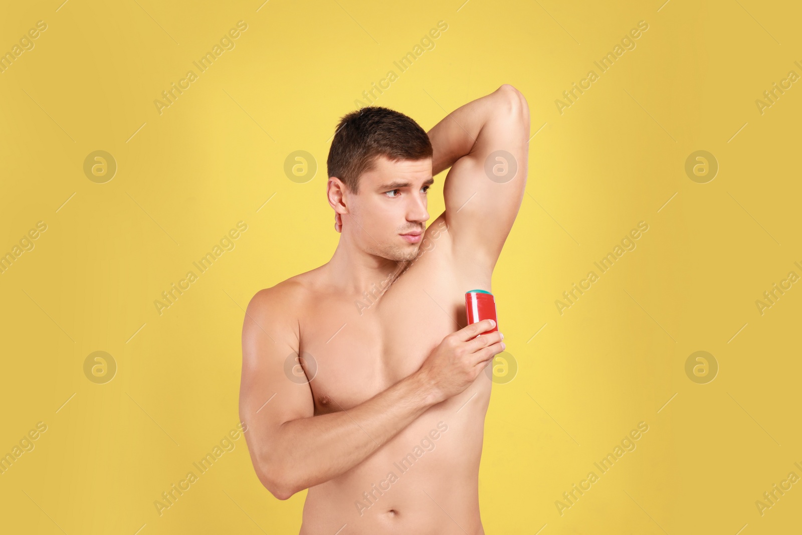 Photo of Young man applying deodorant to armpit on yellow background