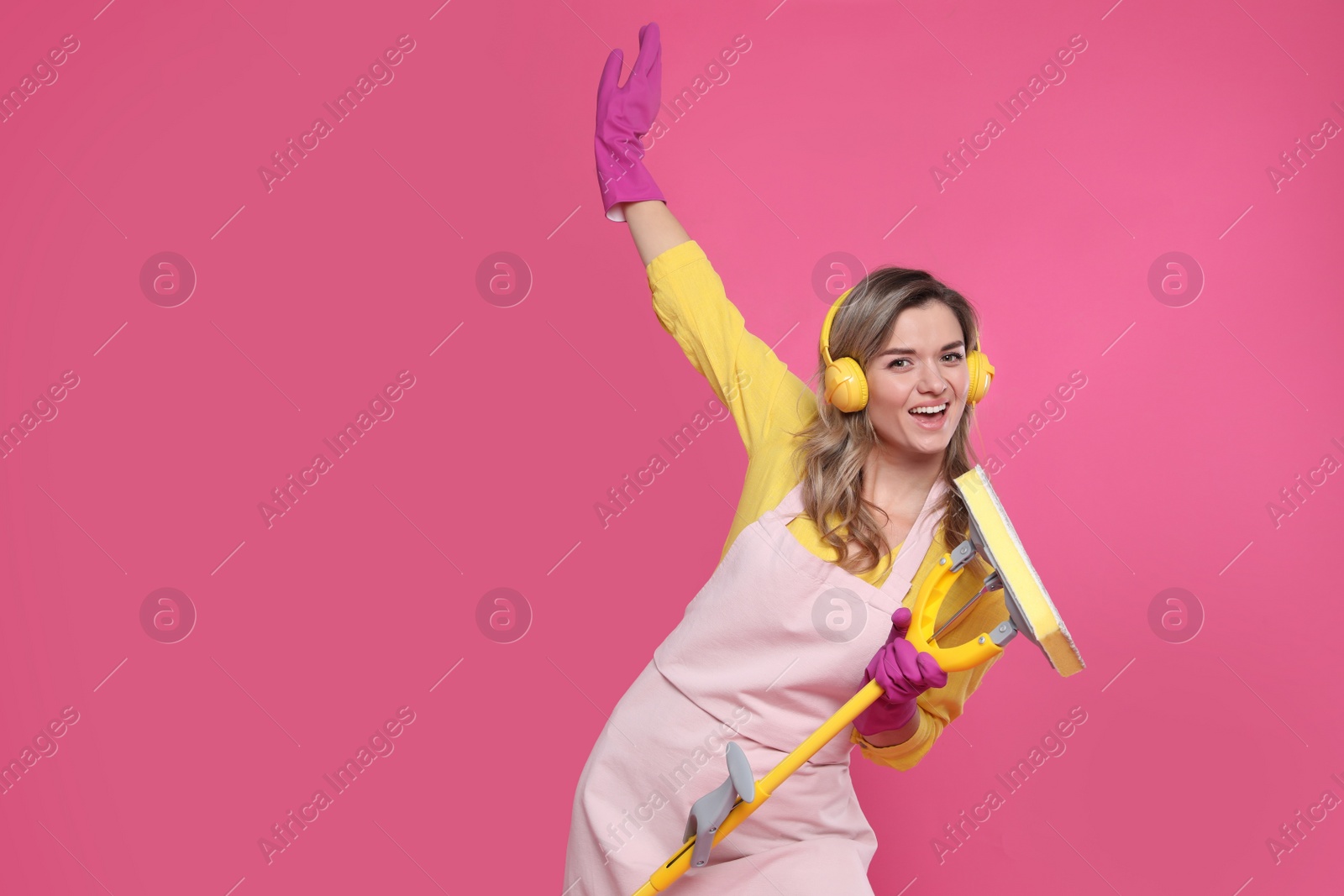 Photo of Beautiful young woman with headphones and mop singing on pink background. Space for text