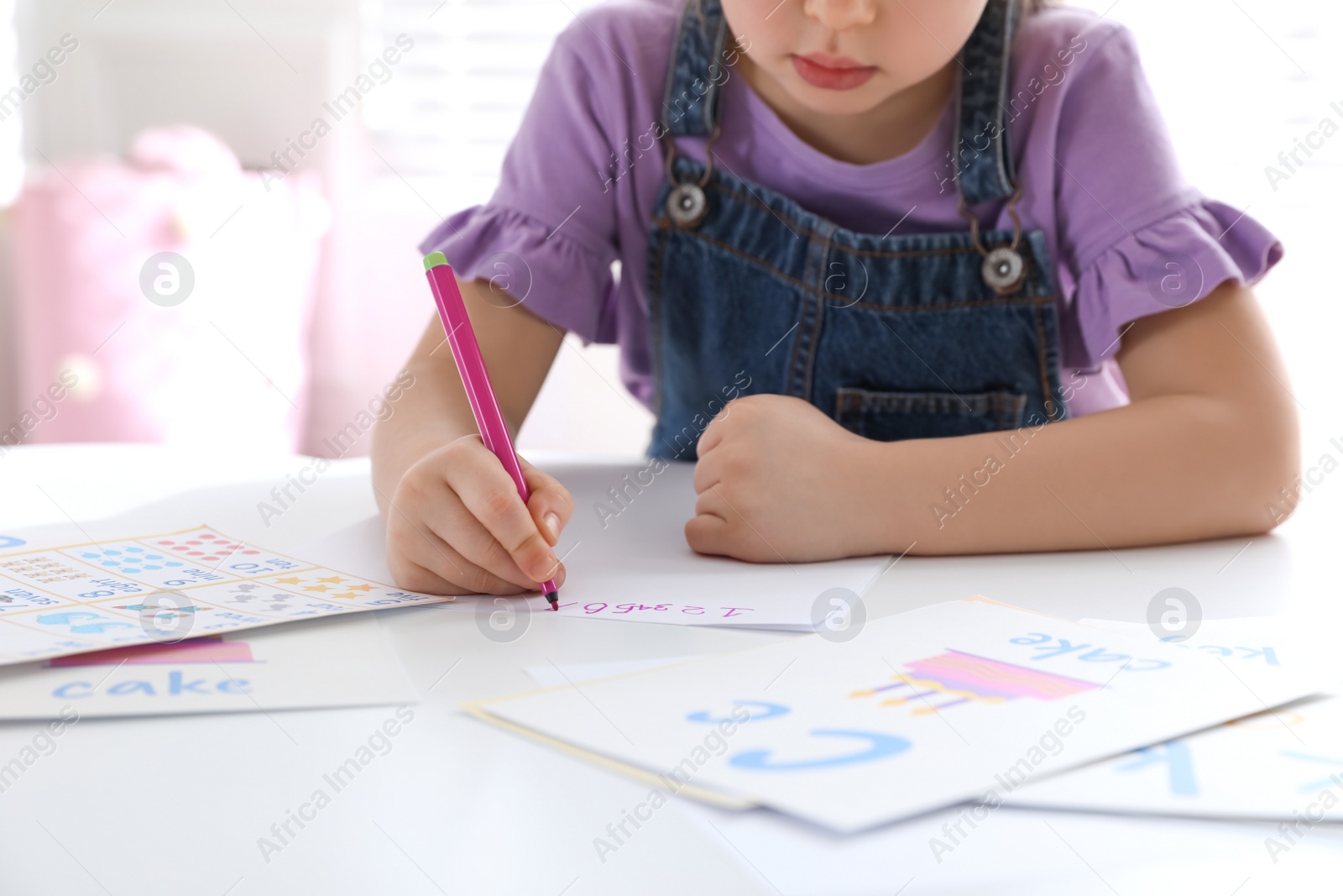 Photo of Little girl writing numbers in classroom at English lesson, closeup