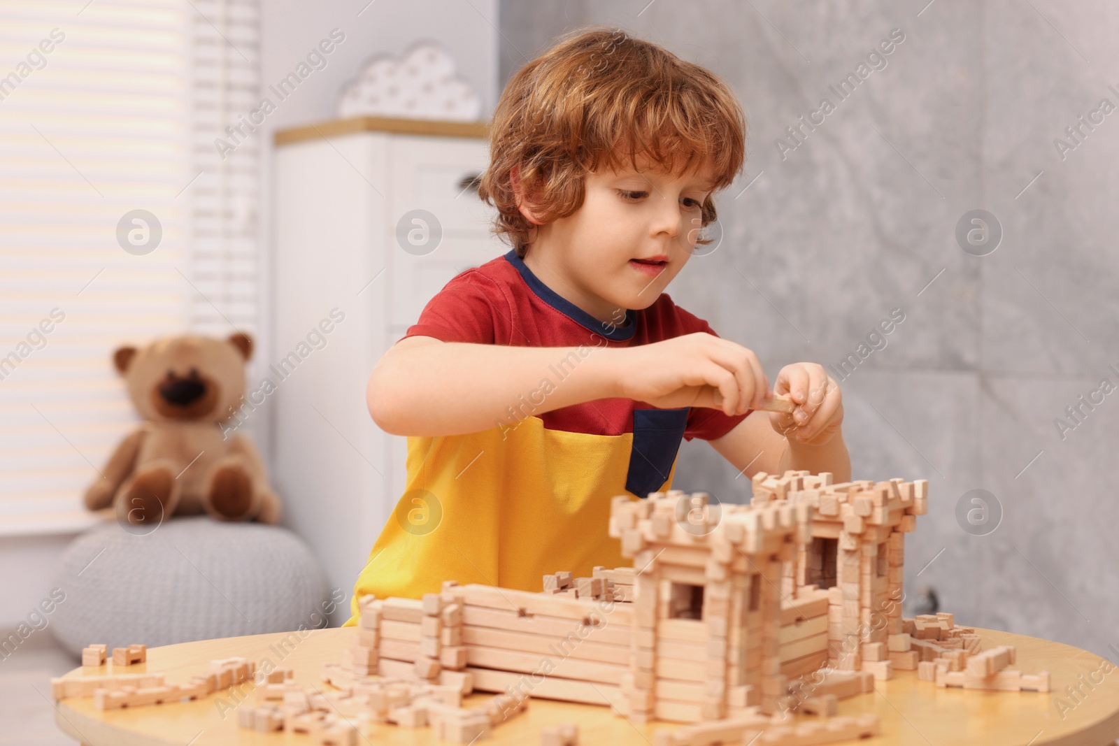 Photo of Cute little boy playing with wooden construction set at table in room. Child's toy