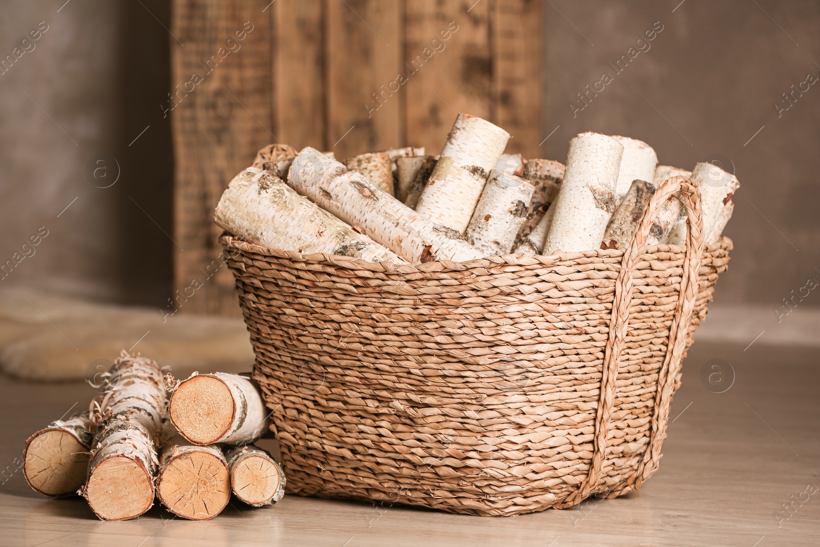 Photo of Wicker basket with cut firewood on floor indoors