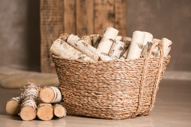 Photo of Wicker basket with cut firewood on floor indoors