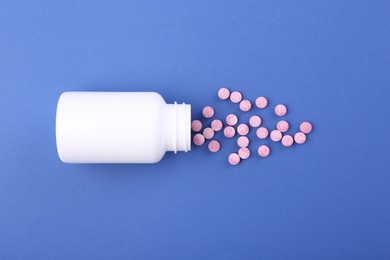 Photo of Bottle and vitamin pills on blue background, top view