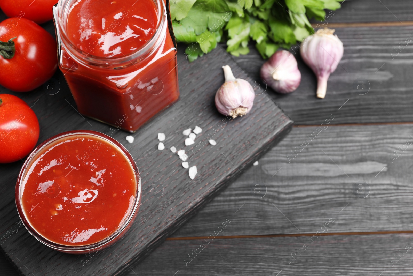 Photo of Flat lay composition with delicious ketchup, spices and products on black wooden table, space for text. Tomato sauce