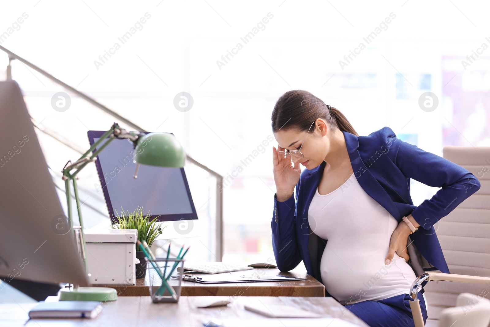 Photo of Young pregnant woman suffering from pain while working in office