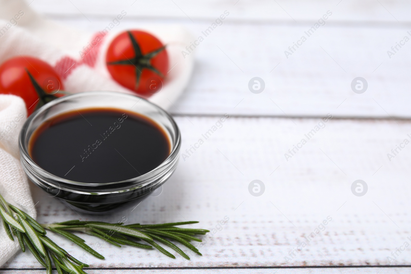 Photo of Bowl with balsamic vinegar, rosemary and tomatoes on white wooden table. Space for text