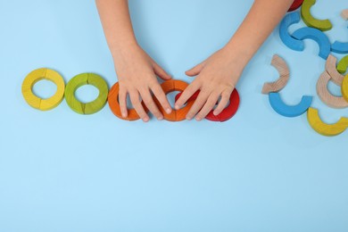 Photo of Motor skills development. Girl playing with colorful wooden arcs at light blue table, top view. Space for text