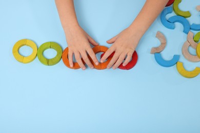 Motor skills development. Girl playing with colorful wooden arcs at light blue table, top view. Space for text