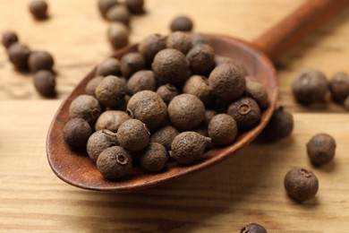 Photo of Dry allspice berries (Jamaica pepper) and spoon on wooden table, closeup