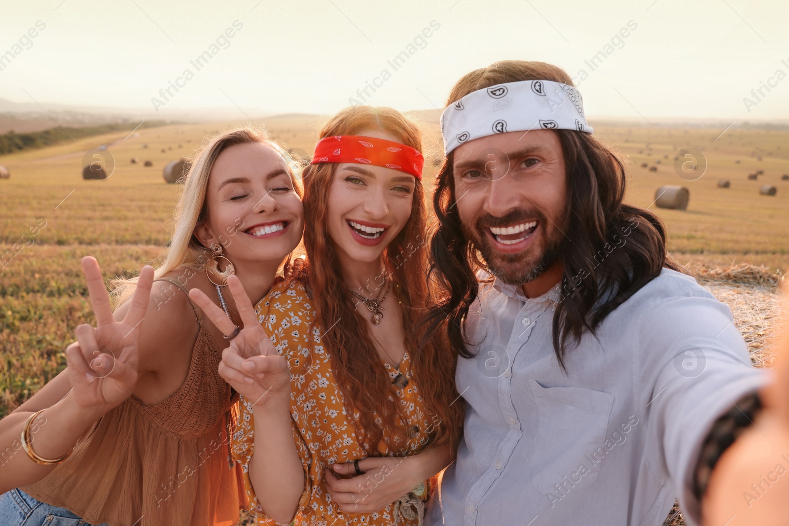 Photo of Happy hippie friends showing peace signs while taking selfie in field