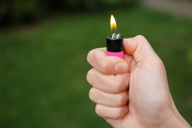 Photo of Man holding lighter with burning flame outdoors, closeup. Space for text