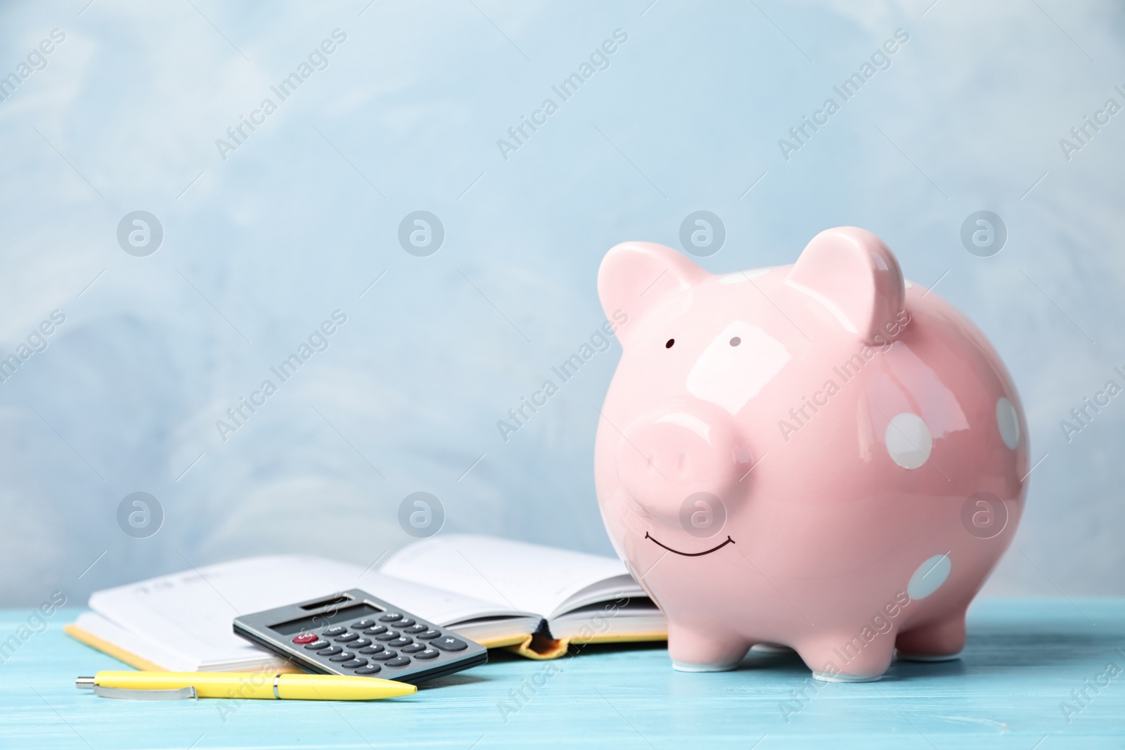 Photo of Piggy bank with calculator and notebook on table. Space for text