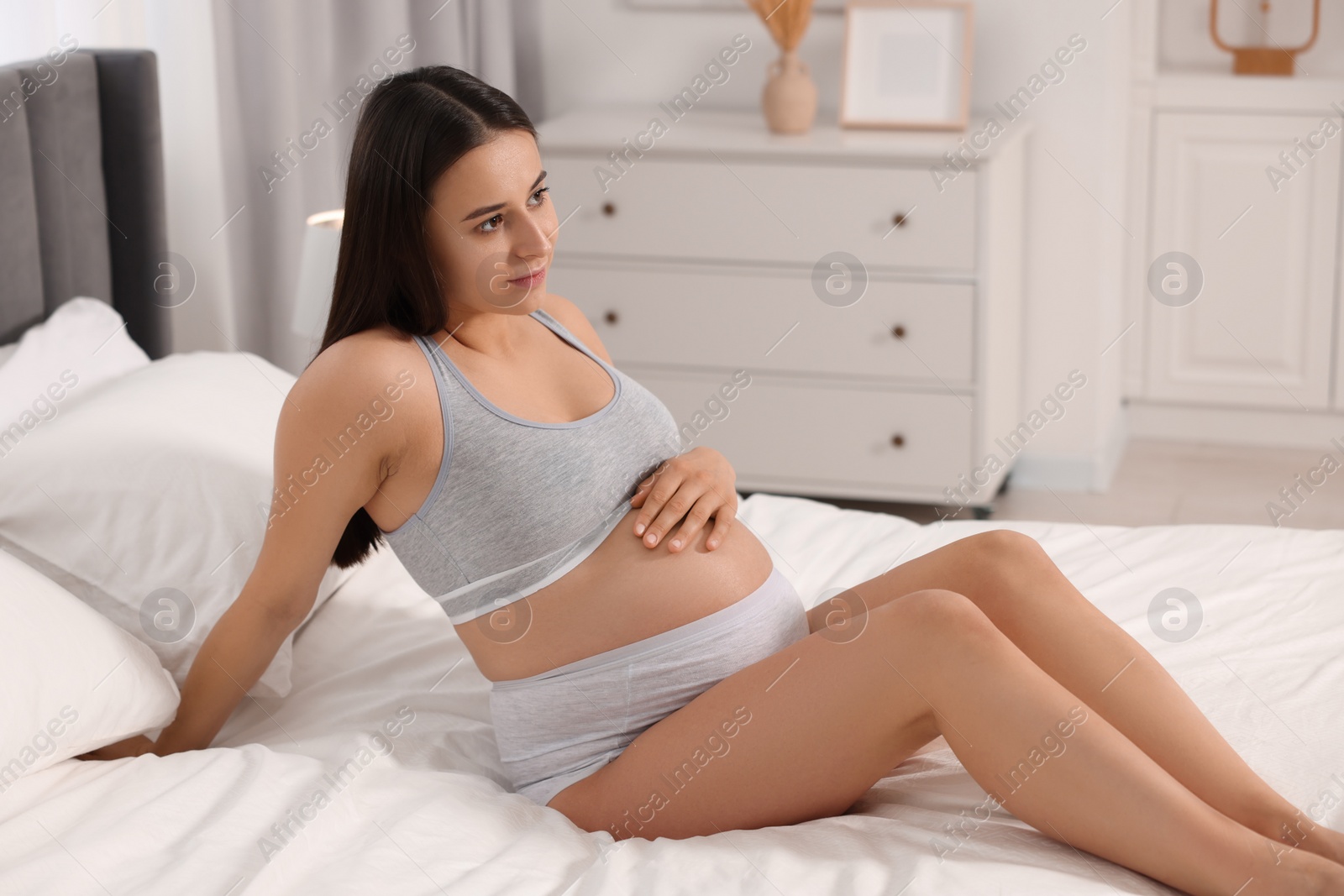 Photo of Beautiful pregnant woman in comfortable maternity underwear on bed at home