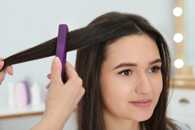 Hairdresser using modern flat iron to style client's hair in salon