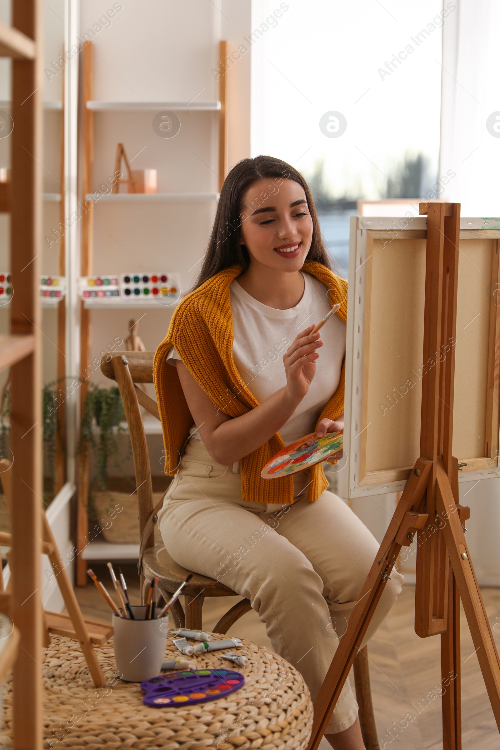 Photo of Beautiful young woman drawing on easel at home