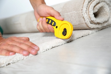 Photo of Man cutting new carpet flooring indoors, closeup. Space for text