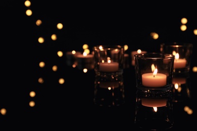Photo of Burning candles in glass holders on dark background. Space for text