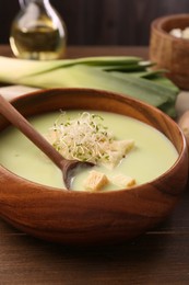 Bowl of tasty leek soup with croutons and spoon on wooden table, closeup