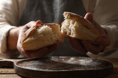 Man breaking loaf of fresh bread at wooden table, closeup