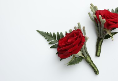 Two stylish red boutonnieres on white background, top view. Space for text