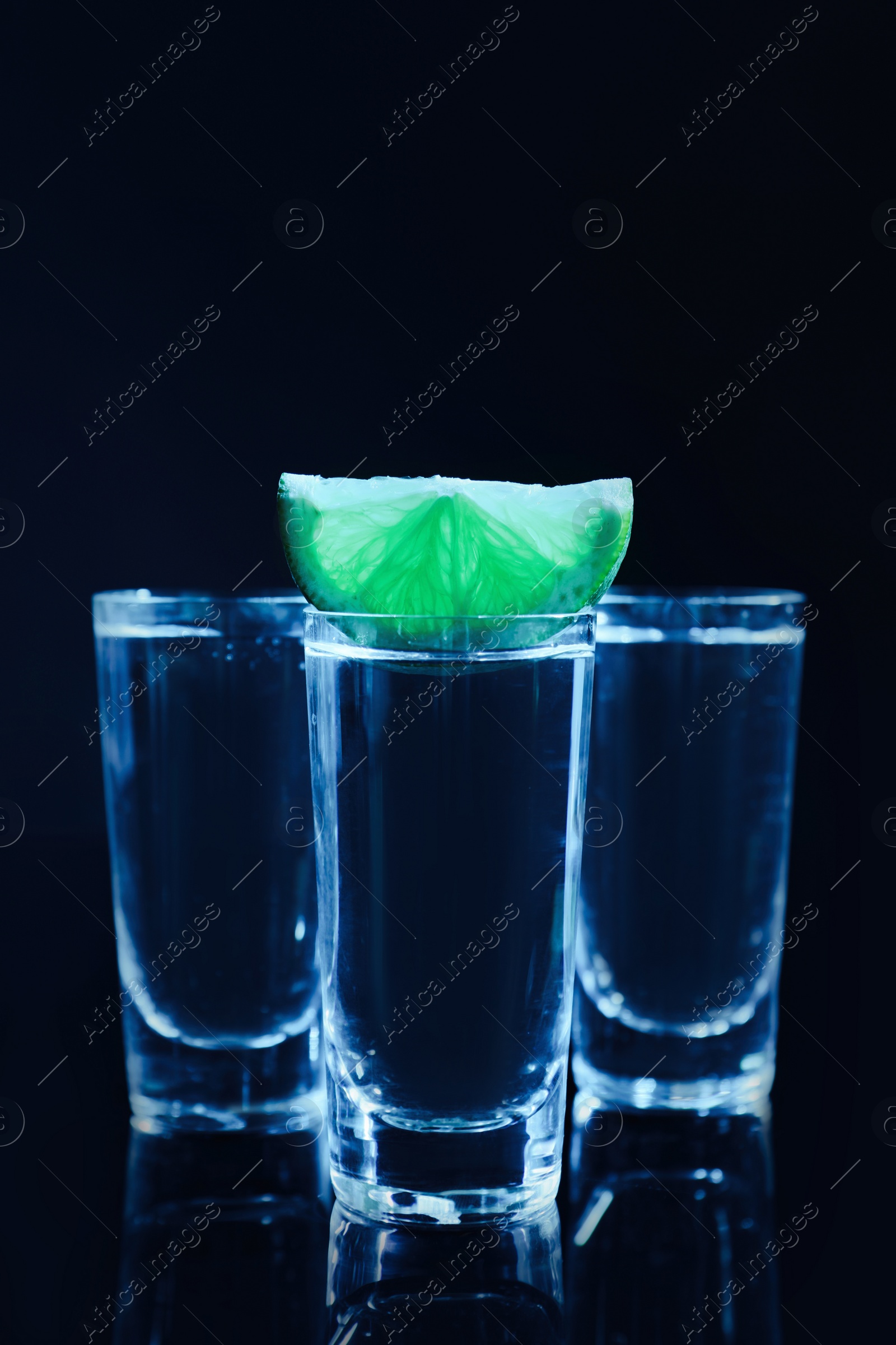 Photo of Shot glasses of vodka with lime slice on dark background