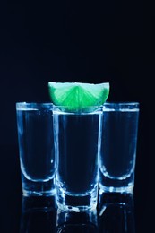 Shot glasses of vodka with lime slice on dark background