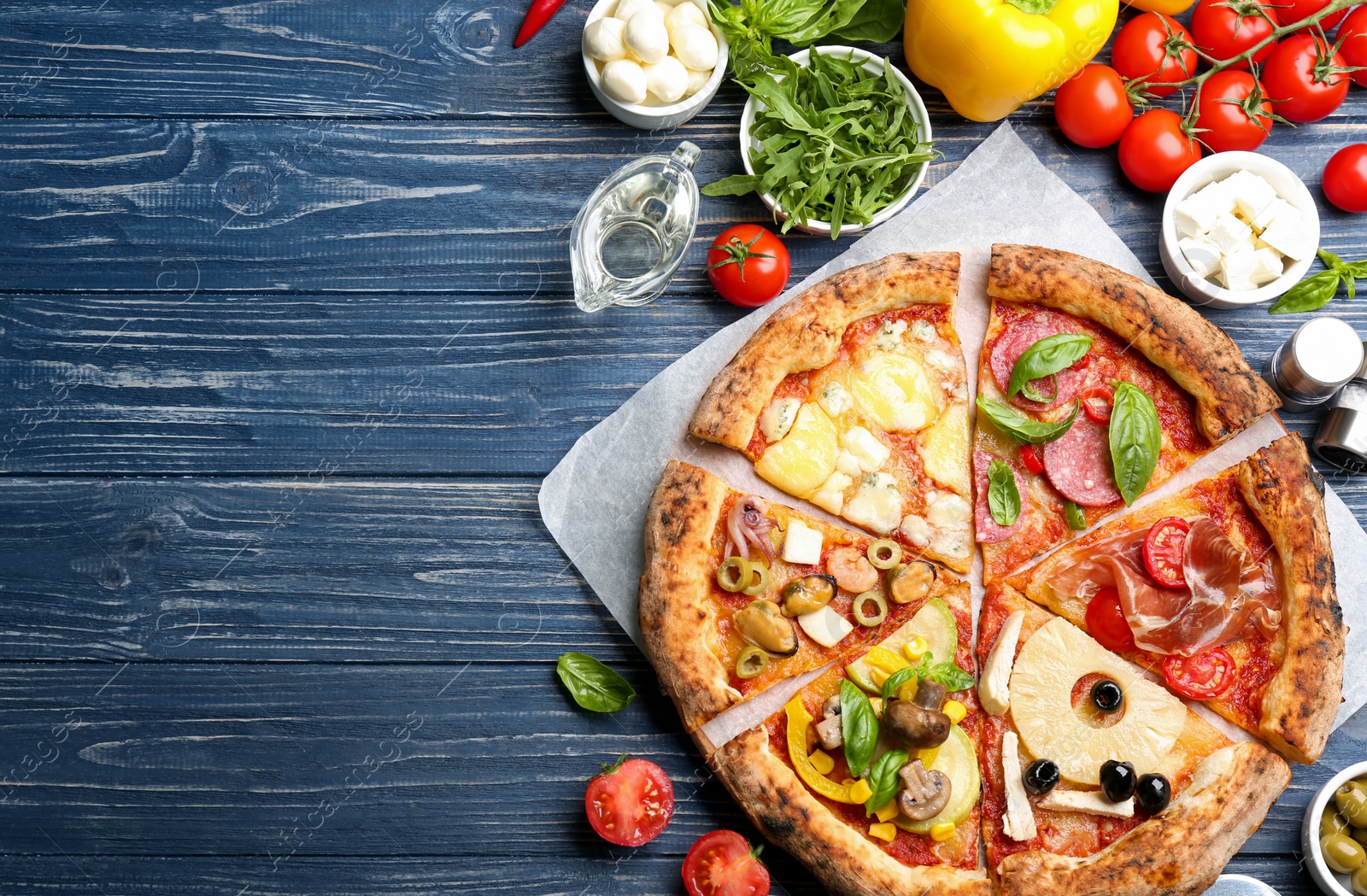 Photo of Slices of different pizzas on blue wooden table, flat lay. Space for text