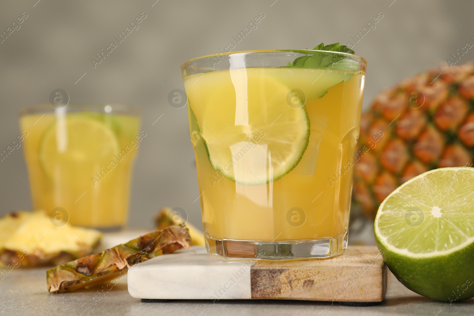 Photo of Glasses of tasty pineapple cocktail with mint and lime on light grey table, closeup