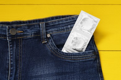 Packaged condoms in jeans pocket on yellow wooden table, top view. Safe sex