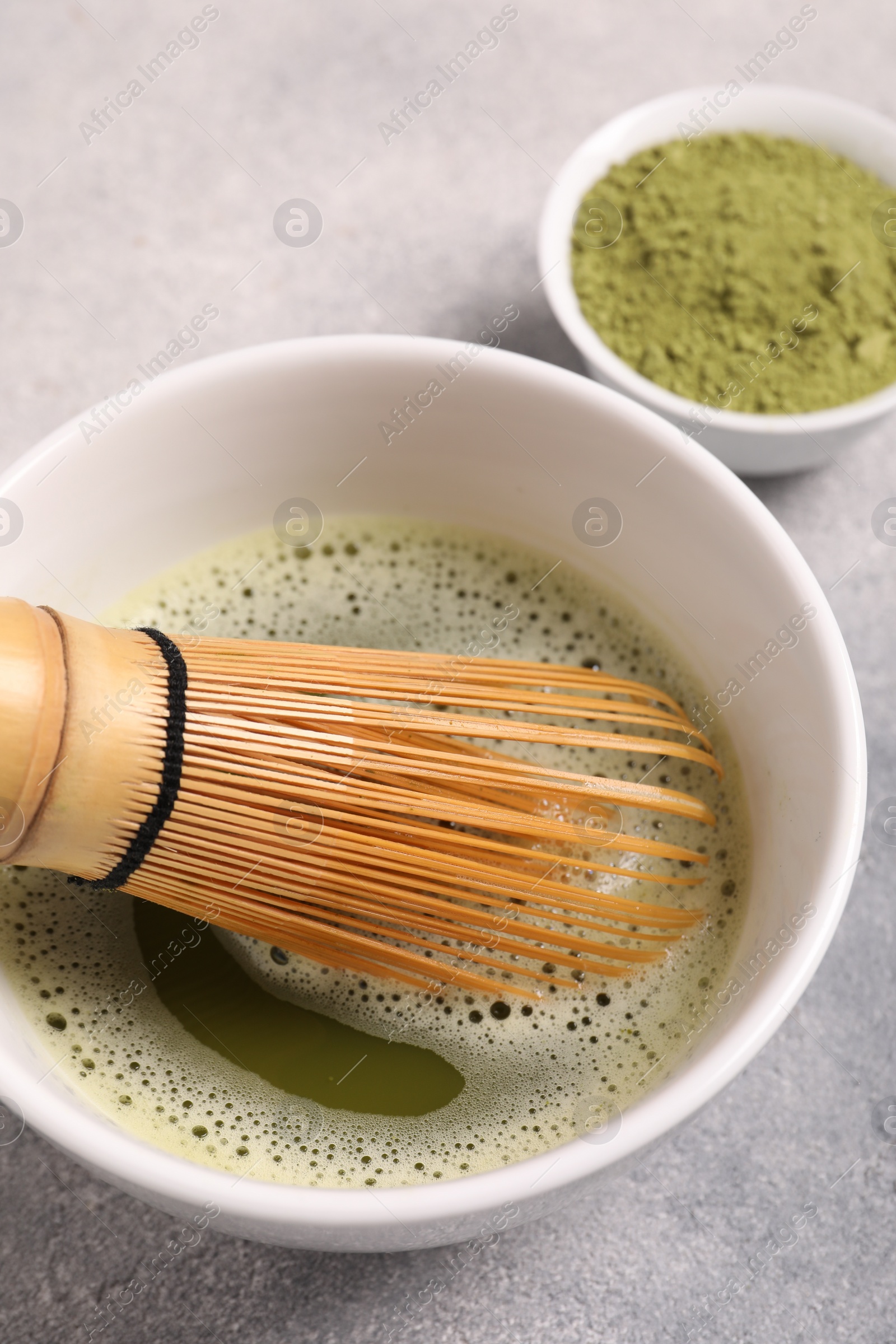 Photo of Cup of matcha tea and bamboo whisk on light gray table, above view