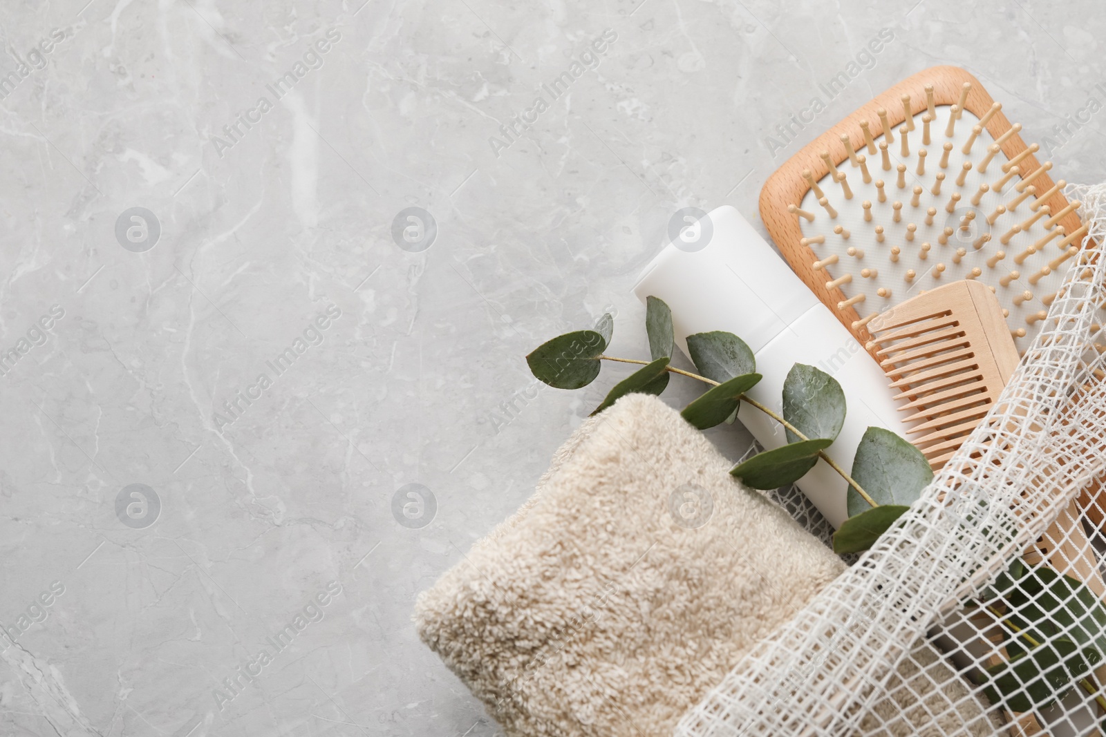 Photo of Dry shampoo spray, towel and hairbrushes with eucalyptus branch on light grey table, top view. Space for text