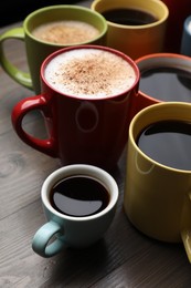 Many different cups with aromatic hot coffee on wooden table