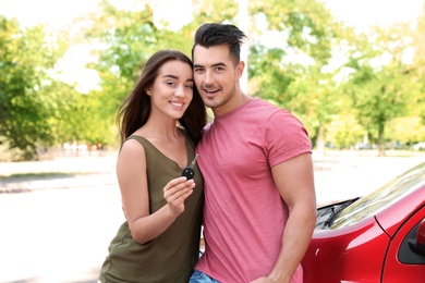 Happy young couple with key standing near new car on road