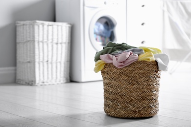 Photo of Wicker basket with dirty laundry on floor indoors, space for text