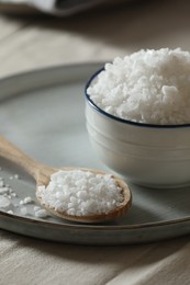 Photo of Organic salt in bowl and wooden spoon on table, closeup