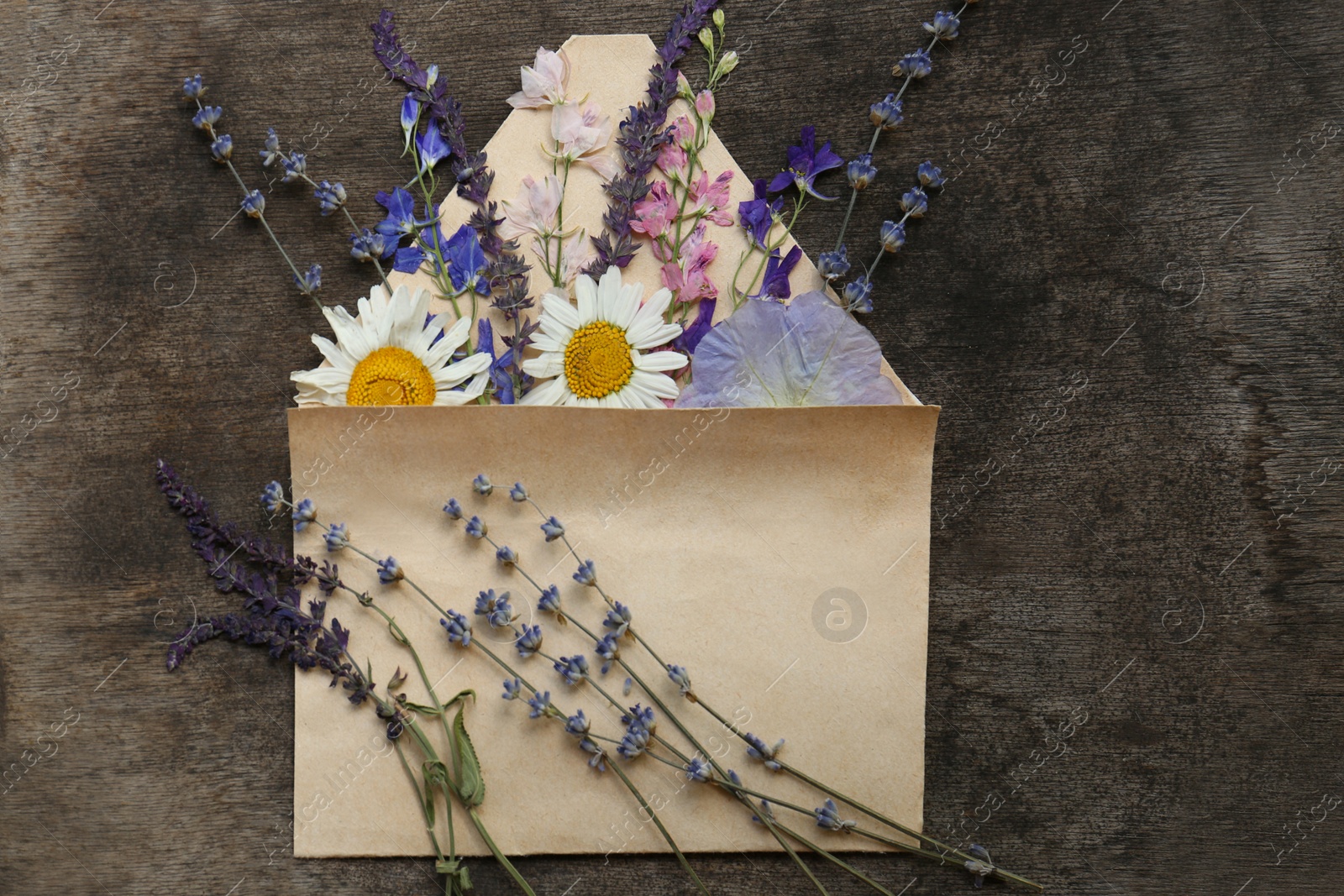 Photo of Flat lay composition with beautiful dried flowers in envelope on wooden background