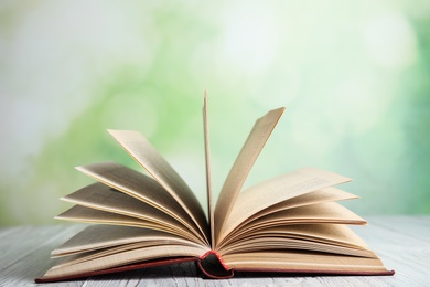 Open book on white wooden table against blurred green background